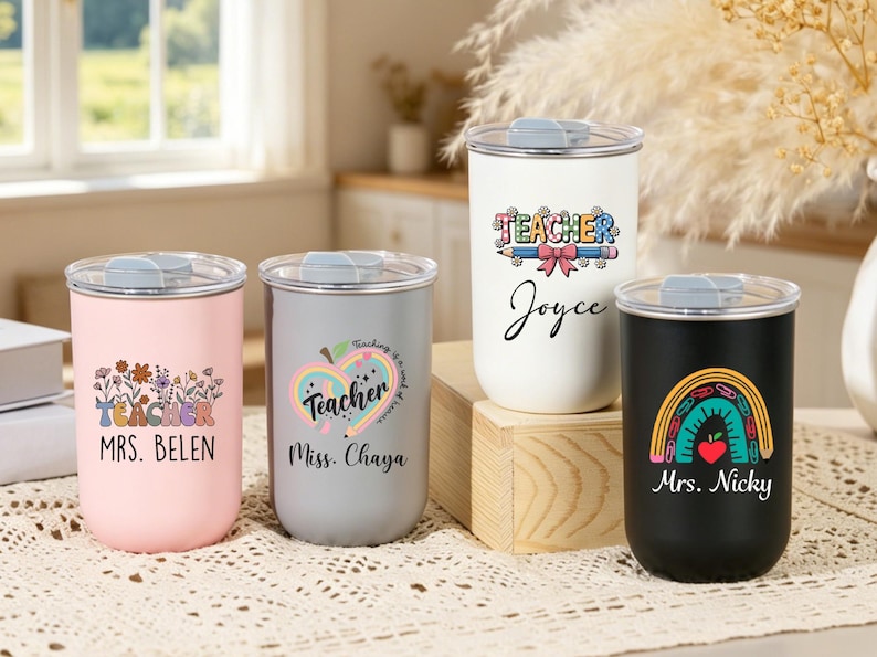May include: Four cylindrical tumblers with clear lids, each featuring unique teacher-themed graphics and names. The colors include pastel pink, light gray, white, and matte black. Each tumbler displays custom text such as Mrs. Belen, Miss. Chaya, Joyce, and Mrs. Nicky.