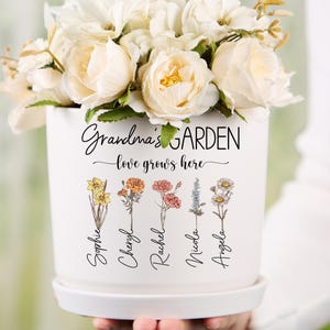 May include: White ceramic planter with the text "Grandma's Garden - love grows here" and five flowers with names "Sophie", "Cheryl", "Rachel", "Nicola", and "Angela" printed below.