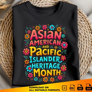 Può includere: T-shirt nero con un design floreale colorato e la scritta "ASIAN AMERICAN AND PACIFIC ISLANDER HERITAGE MONTH." Il testo è in rosso, giallo e blu, circondato da fiori e foglie. La maglietta è presentata su uno sfondo intrecciato.