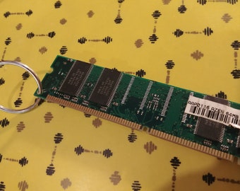 May include: A green circuit board with gold connectors and a black label that reads "AAPD0116 AZEN 64MB PC100". The circuit board is attached to a silver key ring.