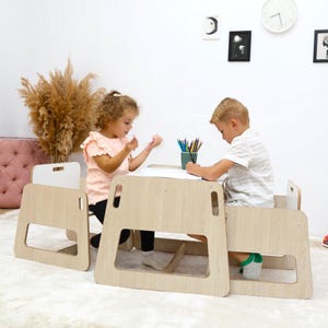 Può includere: Due bambini seduti a un tavolo e sedie di legno, disegnano con matite colorate. Il tavolo e le sedie sono in legno chiaro e hanno un design semplice e moderno.