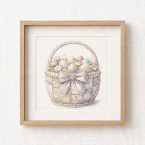 以下が含まれることがあります： イースターエッグと花でいっぱいのバスケットの額入りクロスステッチ。バスケットはラベンダー色で、大きなリボンと真珠のようなトリムが付いています。卵はパステルカラーで、花は白とピンクです。