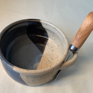 Può includere: Una ciotola in ceramica bianca e nera macchiata con un coltello da burro con manico in legno. La ciotola ha un manico ed è progettata per contenere il burro.