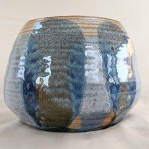 May include: A ceramic bowl with a blue and brown glaze. The bowl has a rounded shape and a wide opening.