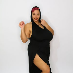 Op de afbeelding: Een vrouw draagt een zwarte jumpsuit met capuchon en een hoge split in het been. De jumpsuit heeft een losse pasvorm en een vloeiende silhouet.