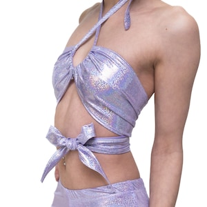 Puede incluir: Un top halter de color lavanda con un acabado iridiscente brillante. El top tiene un diseño envolvente y se ata en la parte delantera. El top está hecho de una tela elástica y cómoda.
