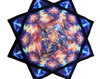 May include: A colorful tapestry with a geometric design featuring a starburst pattern and a galaxy-like print. The tapestry has a black border.