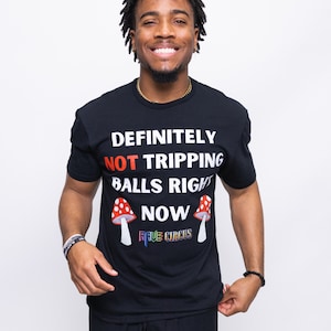 May include: Black t-shirt with the text "DEFINITELY NOT TRIPPING BALLS RIGHT NOW" and two red and white mushroom graphics. The shirt also features the text "RAVE CIRCUS" in rainbow colors.