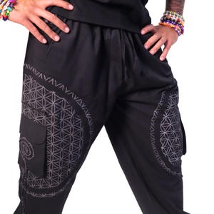 Op de afbeelding: Zwarte broek met een geometrisch patroon op de benen. Het patroon is een wit levensbloemontwerp.