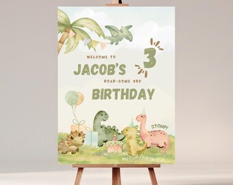 Op de afbeelding: Verjaardagsbord op een ezel met een aquarelontwerp. Het bord luidt "Welkom op Jacobs 3e verjaardag" met dinosaurusillustraties, ballonnen en een palmboom. Het kleurenpalet omvat groen, roze en beige.