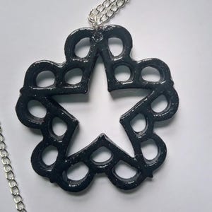 May include: A black necklace with a star-shaped pendant. The pendant is made of a black material with a glittery finish and has a cutout design.