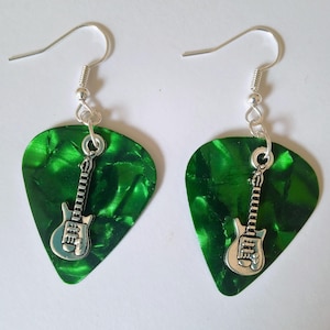 Op de afbeelding: Een paar gitaar plectrum oorbellen. Elke oorbel heeft een getextureerde, smaragdgroene plectrum met een zilverkleurige gitaarbedel. De oorbellen hebben zilverkleurige oorhaken.