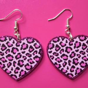 May include: A pair of pink heart-shaped earrings with a leopard print design. The earrings have silver hooks.