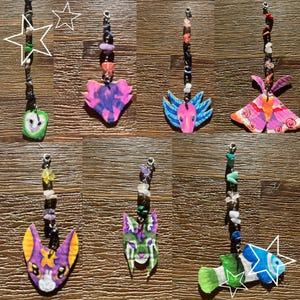 May include: A collection of handmade gemstone and charm pendants. Each pendant features a unique design, including a heart, butterfly, moth, cat, and fish, all painted in vibrant colors. The pendants are strung with a variety of colorful gemstones.