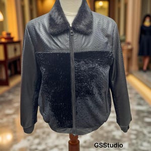 Puede incluir: Chaqueta negra con un estampado de piel de serpiente sintética en la parte superior y las mangas. La chaqueta presenta un panel oscuro y afelpado en el pecho y un cuello de piel. La chaqueta está abrochada con cremallera y se exhibe en un maniquí.