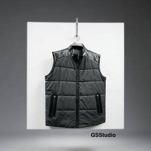 Pode incluir: Um colete preto acolchoado com gola alta e zíper completo. Os ombros e os acabamentos dos bolsos apresentam um material escuro e texturizado. O colete está pendurado em um cabide contra um fundo branco. O texto "GSStudio" é visível na parte inferior.