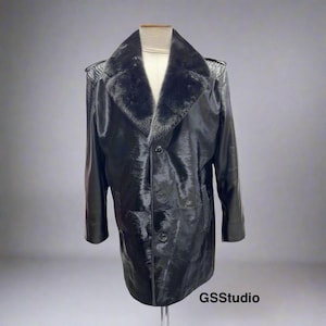 Pode incluir: Um casaco preto, até ao joelho, com gola e lapelas de pele sintética. O casaco tem um acabamento brilhante, três botões e um padrão texturizado nos ombros. O casaco é exibido num manequim.