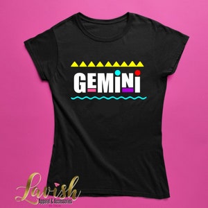 May include: Black t-shirt with a white graphic that says "GEMINI" in colorful block letters. The graphic is surrounded by yellow triangles, a blue wavy line, and colorful dots.