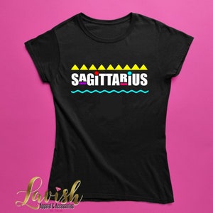 May include: Black t-shirt with a yellow, blue, red, and purple graphic that says "SAGITTARIUS" with a row of yellow triangles above the text and a wavy blue line below the text.