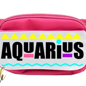 May include: A pink fanny pack with a white patch that says "AQUARIUS" in black letters with colorful accents. The patch has a yellow, blue, and pink geometric design.