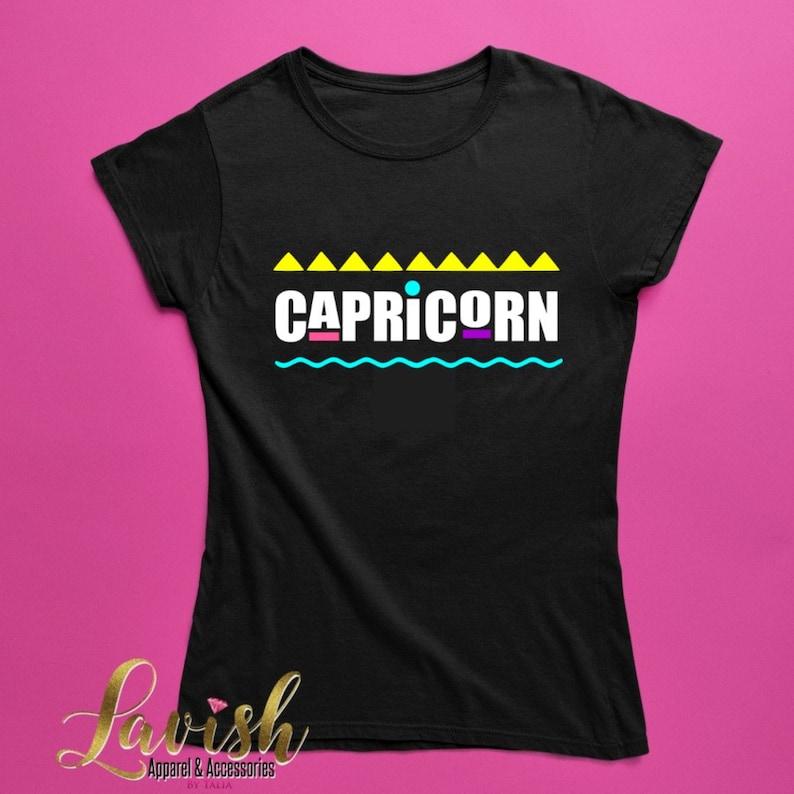 May include: Black t-shirt with a graphic design featuring the word "CAPRICORN" in colorful letters with a blue wavy line and yellow triangles above the word.