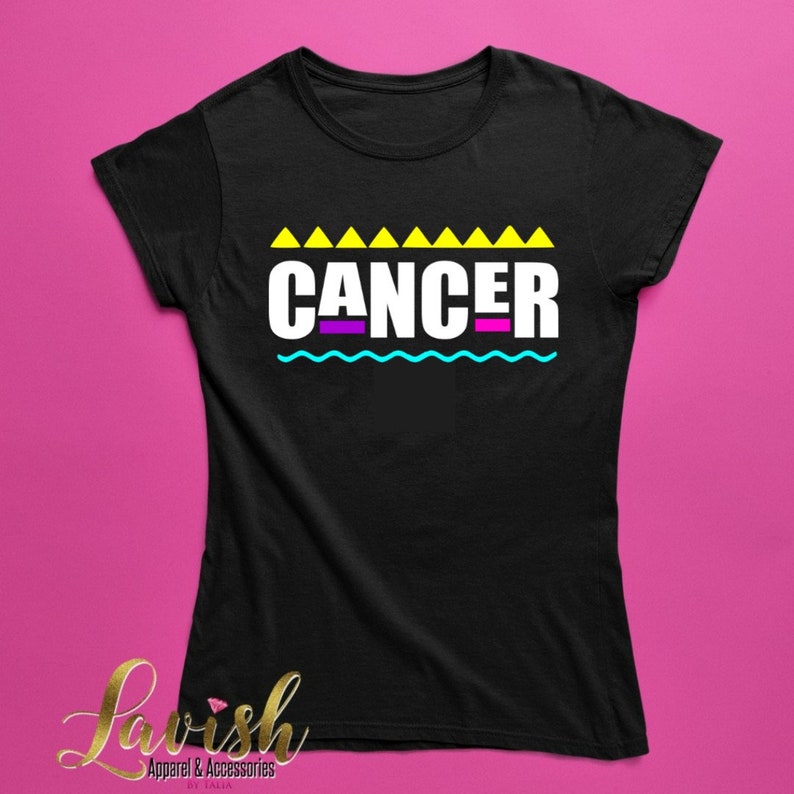 May include: Black t-shirt with a white graphic that says "CANCER" in yellow, purple, and blue letters. The graphic is surrounded by yellow triangles and a blue wavy line.