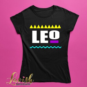 May include: Black t-shirt with a white graphic of the word "LEO" in a retro 90s style. The graphic features yellow triangles, a purple line, and a blue wavy line.