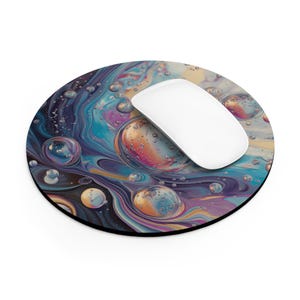May include: Round mousepad with a vibrant, abstract design featuring swirling blues, purples, and oranges, resembling bubbles or a fluid galaxy. A white computer mouse rests on the pad, providing a functional and artistic workspace accessory.