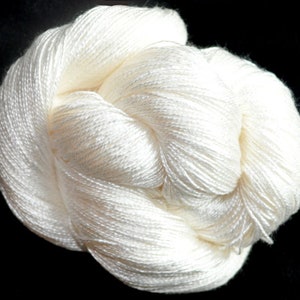 May include: A skein of white yarn, made of silk, is shown in a close-up view. The yarn is soft and delicate, and it is perfect for knitting or crocheting.