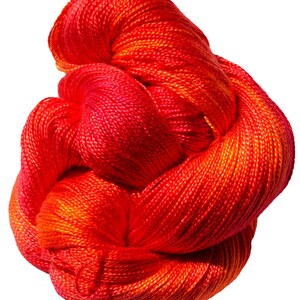 May include: A skein of red and orange yarn with a gradient effect. The yarn is twisted and knotted, showing the texture of the fibres.
