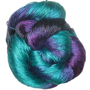 May include: A ball of yarn in teal, purple, and black hues. The yarn has a fine, smooth texture, possibly silk or a silk blend. The colours are blended, creating a gradient effect. The yarn is tightly wound into a ball.