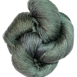 May include: A ball of yarn in muted green and grey tones, tightly wound. The yarn has a slight sheen, possibly indicating a mixed fibre composition. The texture looks soft, ideal for knitting or crochet. The yarn is set against a white backdrop.