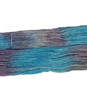 May include: A long, thin, woven strip of fabric with a gradient of blue, purple, and white colors. The fabric has a wavy texture.