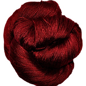 May include: A ball of crimson yarn, tightly wound and textured. The yarn appears to be a rich, solid colour, with subtle variations in tone. The image is a close-up, highlighting the intricate weave and the luxurious appearance of the material.