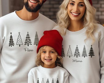 May include: A family wearing matching white sweatshirts and red beanies. Each sweatshirt features a row of black Christmas tree designs. The sweatshirts are labeled "Papa", "Mama", and "Mini".