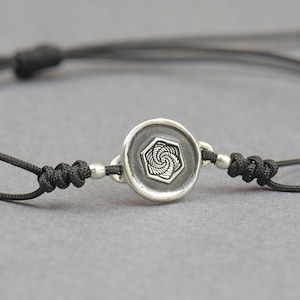 Può includere: Un braccialetto in corda nera con un ciondolo d'argento con un design geometrico.