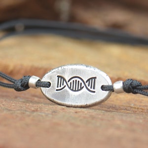 May include: A black cord bracelet with a silver oval charm featuring a DNA double helix design.