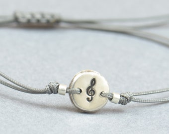 Peut inclure: Un bracelet ajustable gris avec un charme argenté en forme de clé de sol.