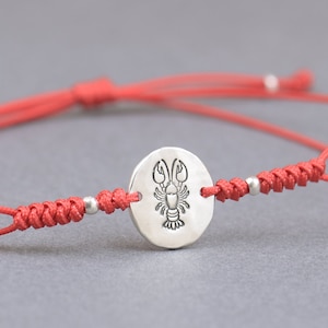 May include: Red string bracelet with a silver charm featuring a lobster design.