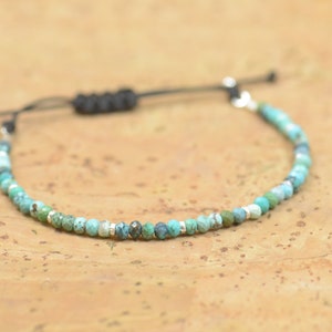 May include: A turquoise and silver beaded bracelet with a black cord adjustable closure.