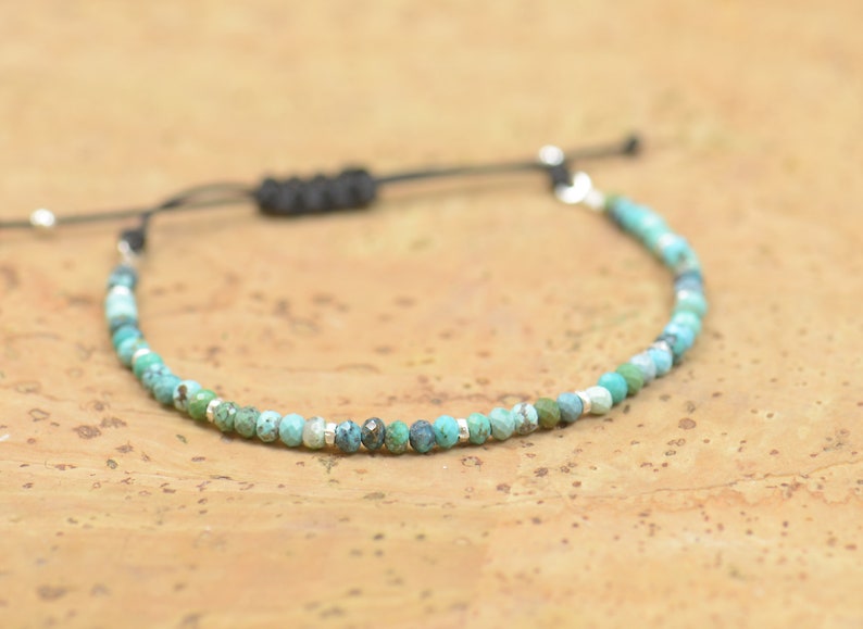 May include: A turquoise and silver beaded bracelet with a black cord adjustable closure.