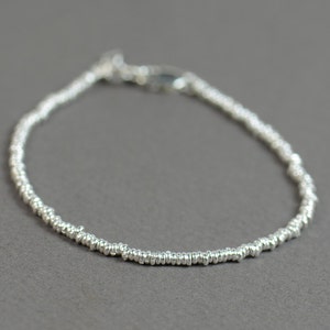 Puede incluir: Un brazalete de plata hecho de pequeños anillos unidos.