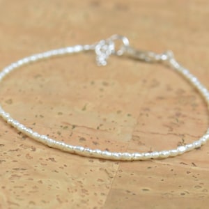 Peut inclure: Un bracelet délicat en perles blanches avec un fermoir argenté.