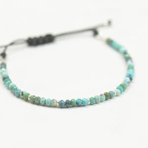 May include: A turquoise and silver beaded bracelet with a black cord closure.