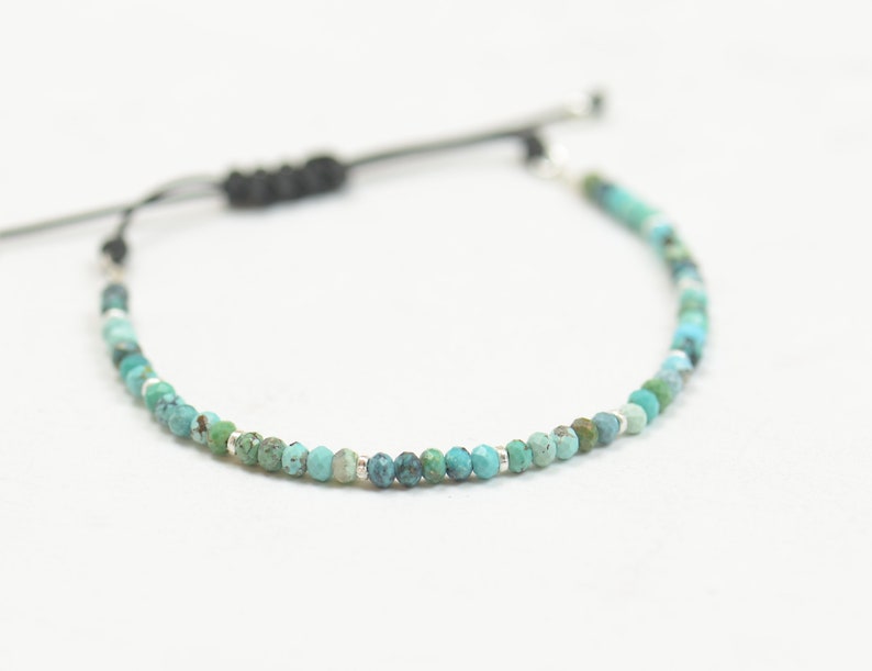 May include: A turquoise and silver beaded bracelet with a black cord closure.
