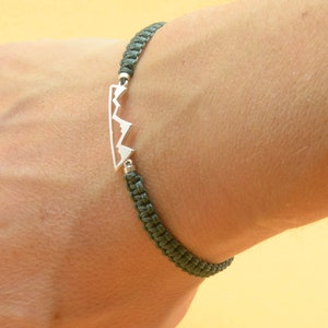 May include: A green cord bracelet with a silver mountain range charm.
