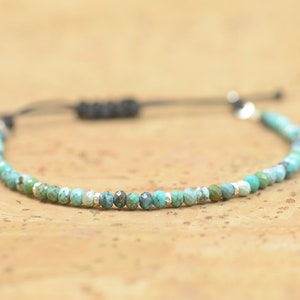May include: A turquoise and silver beaded bracelet with a black cord and adjustable closure.
