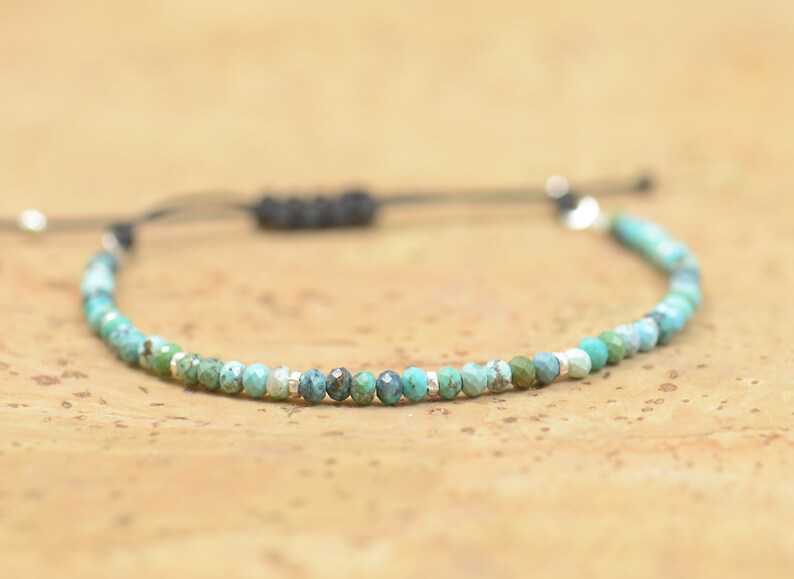 May include: A turquoise and silver beaded bracelet with a black cord and adjustable closure.