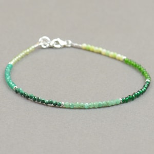 May include: A delicate green gemstone bracelet with a silver clasp. The bracelet features a gradient of green beads, starting with light green and transitioning to dark green.
