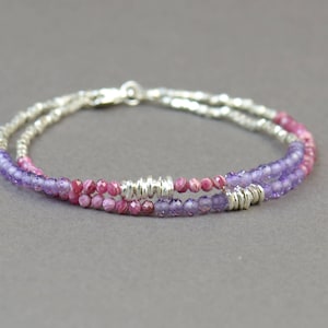 May include: A silver bracelet with two rows of beads. The top row is made of pink and white striped beads, and the bottom row is made of purple beads.